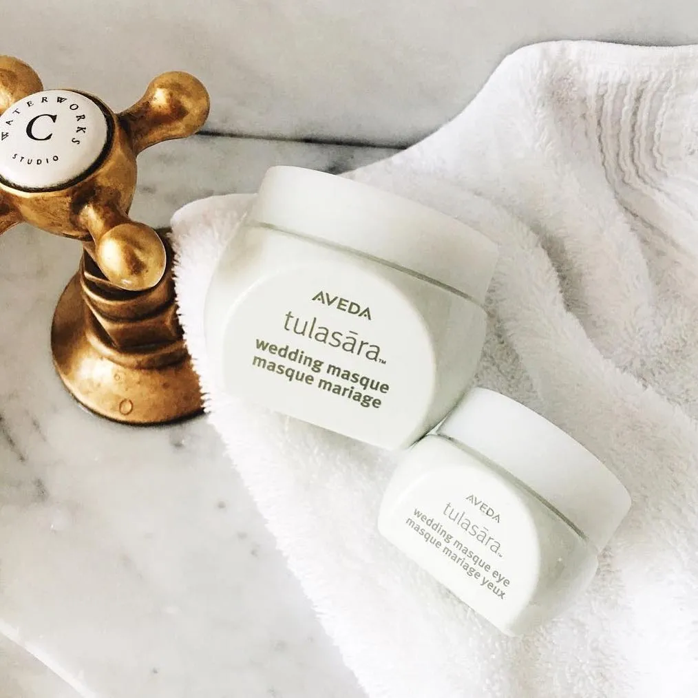 Masques visage Aveda Tulasara disposés sur des serviettes blanches avec un outil de massage doré.