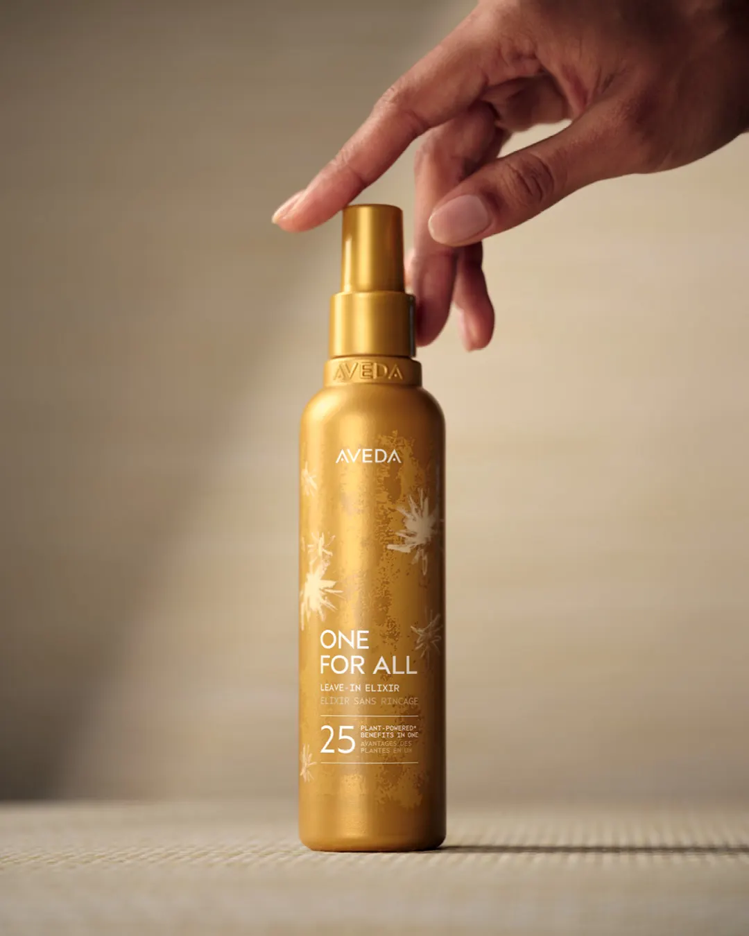 Flacon doré Aveda One for All, un élixir sans rinçage pour les cheveux, tenu par une main