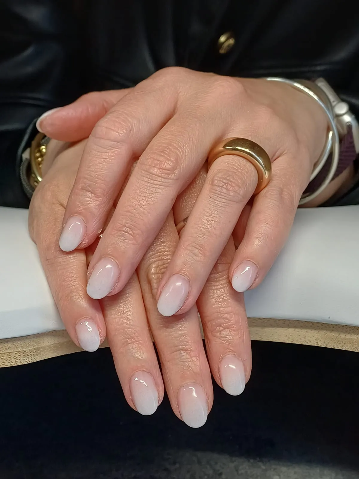 Mains entrecroisées avec une manucure ovale blanc rosé et des bijoux