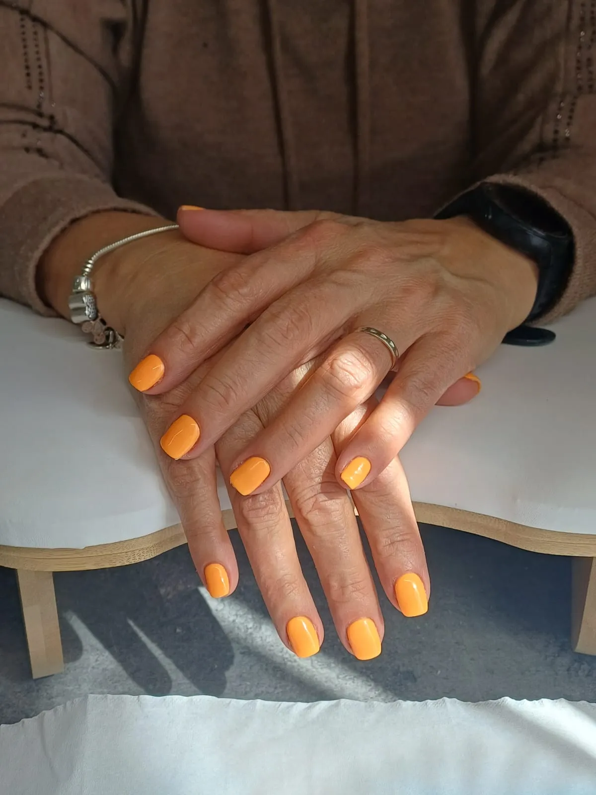 Ongles courts vernis d’un orange vif, mains posées sur une table de soin
