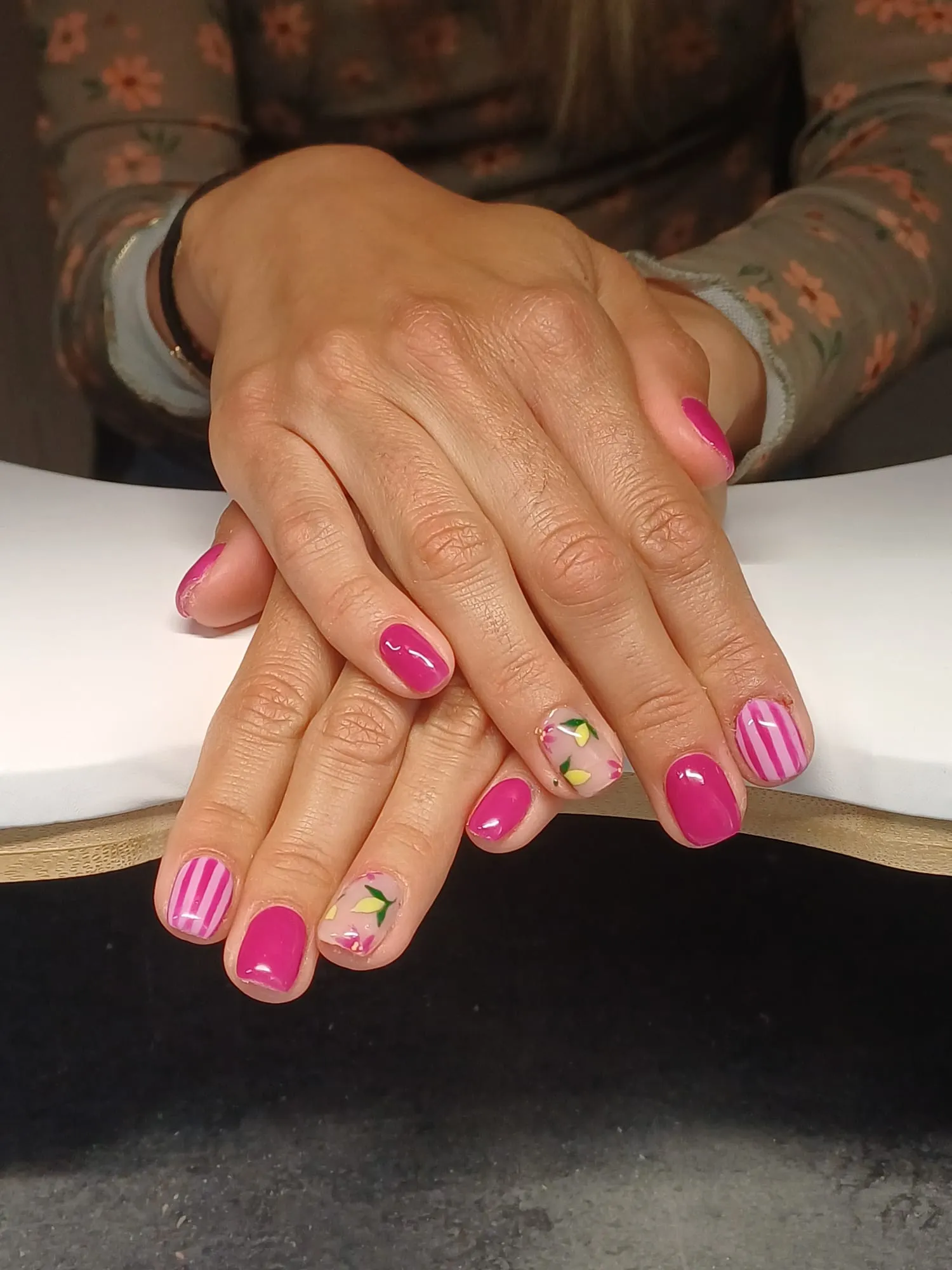 Mains aux ongles rose vif décorés de motifs floraux et de rayures
