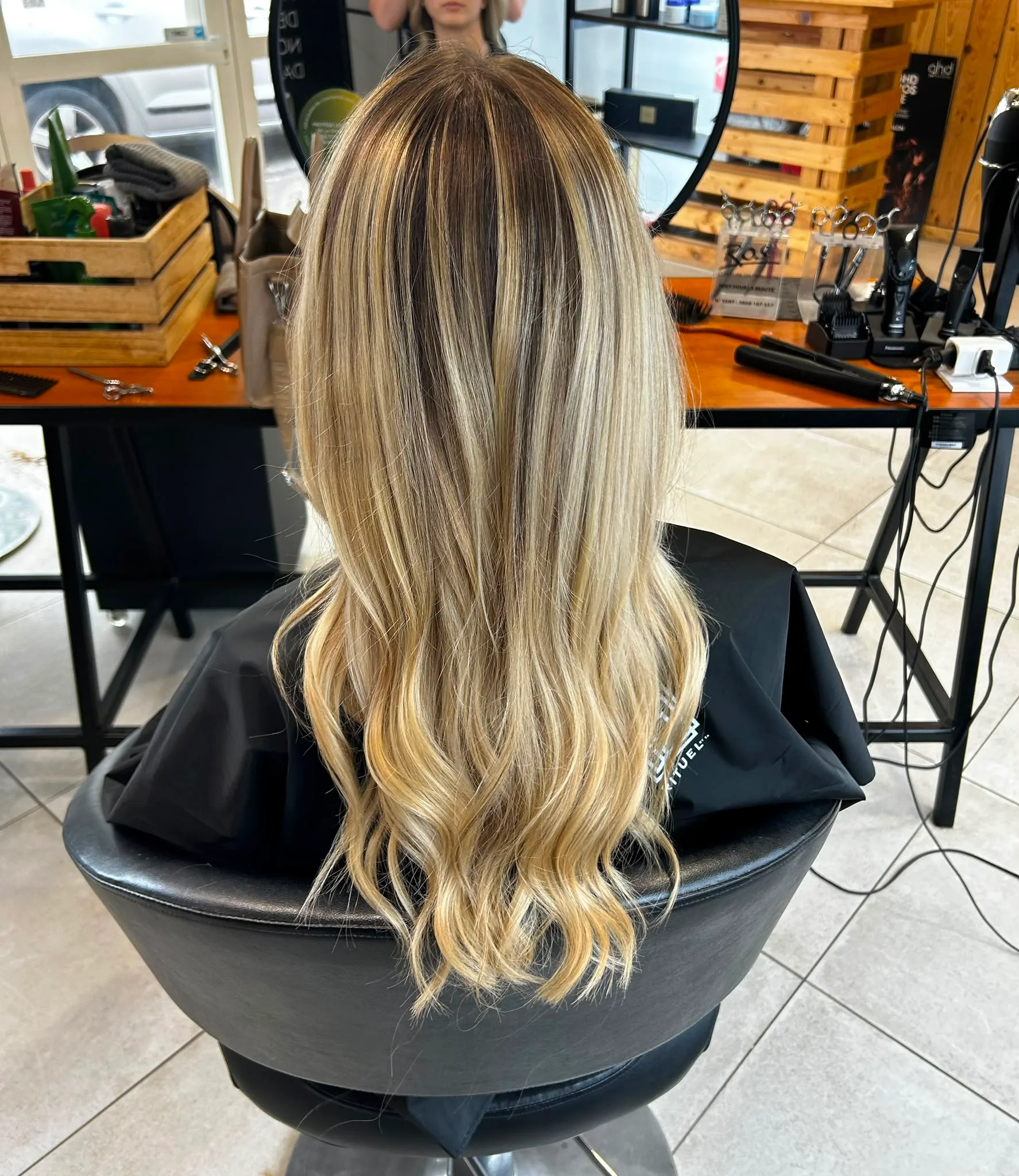 Chevelure longue ondulée vue de dos, aux racines brunes et aux mèches blondes lumineuses